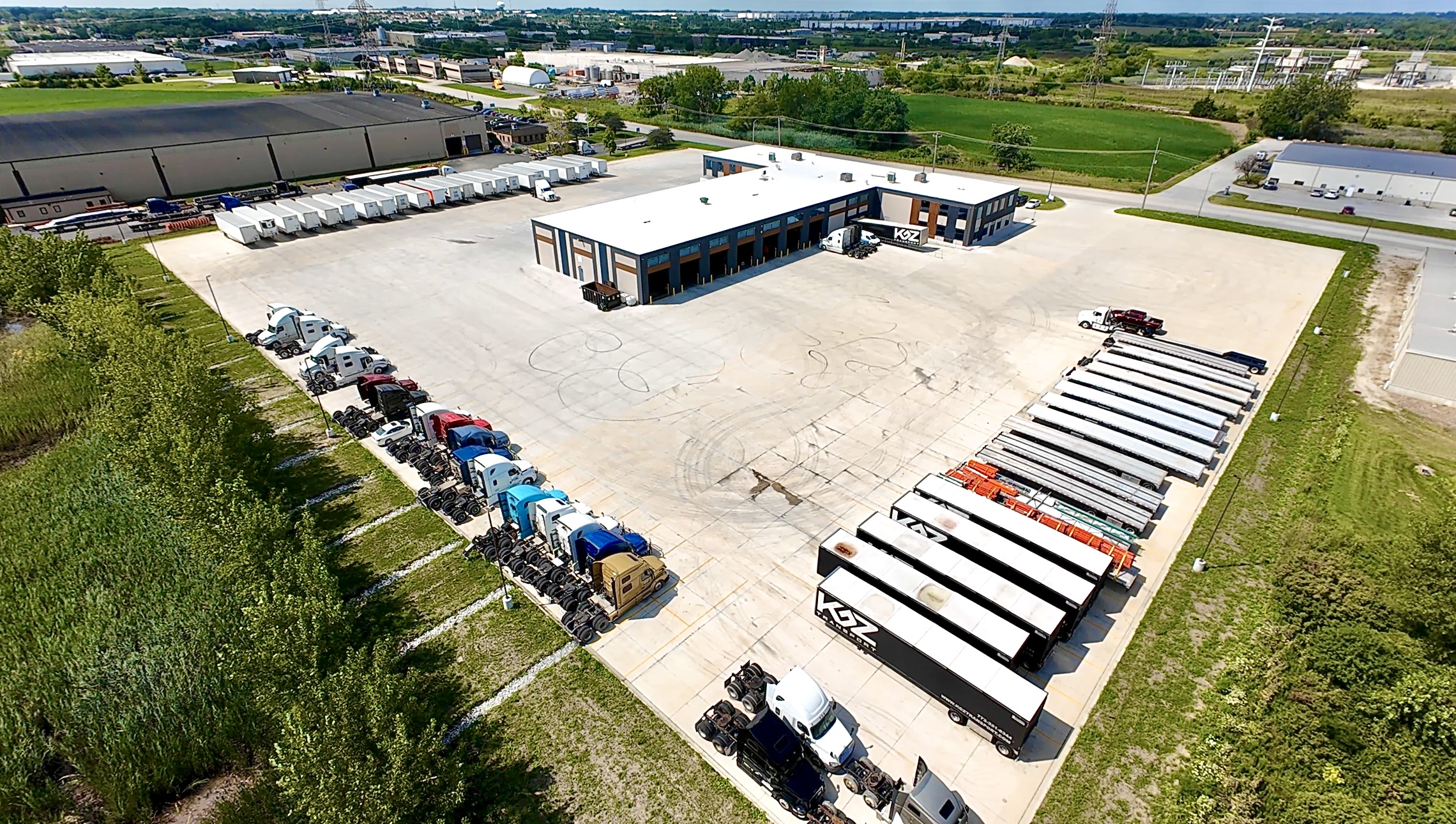 Aerial view of the KGZ Transport headquarters in University Park, Illinois — main shop and office building with a full lineup of KGZ tractors and trailers in the lot